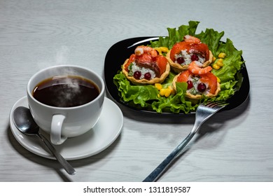 Sample breakfast consisting of a snack with red fish and a cup of hot coffee on a wooden table.