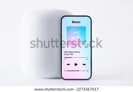 Sample music player app on mobile phone in front of wireless speaker on white background