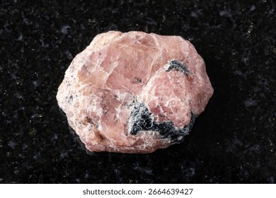 sample of raw pink ruby mineral on black granite background close up