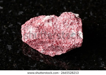 sample of rough cinnabar rock on black granite background close up from Kyrgyzstan