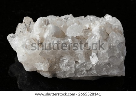 sample of rough druse of clear quartz rock on black granite background close up from China