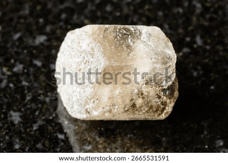 sample of rough phenakite stone on black granite background close up from Middle Urals, Russia