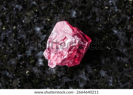 sample of rough red spinel crystal on black granite background close up from Myanmar