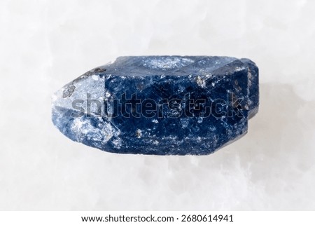 sample of rough single blue sapphire crystal on white marble background close up from Tanzania