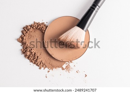A sample of a round block of compact powder in a brown tone and a chic brush for applying makeup. loose powder sample. top view. layout for design