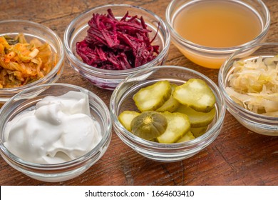 a sampler of fermented, prebiotics, food great for gut health - glass bowls against wood:  kimchi, red beets, apple cider vinegar, coconut milk yogurt, cucumber pickles, sauerkraut