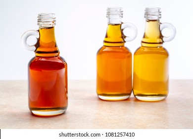 sampler of pure maple syrup (golden, amber and gold) - three small glass bottles on a ceramic background