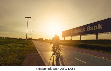 SAMUT PRAKAN, THAILAND-JUNE 18, 2021 : Sports man ride bicycles on the road in the evening near Bangkok Bank advertising billboard with sunset sky. Summer outdoor exercise for healthy and happy life.