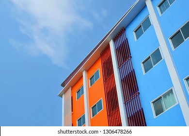 Samutsakhon, Thailand - February 6,2019 : Low angle view of colorful blue and orange building with windows and balusters lines pattern in modern style against cloud and blue sky background in the city