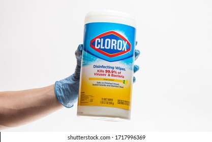 SAN ANTONIO, TEXAS - 04/29/2020 - Woman Hand Wearing Surgical Protective Glove Holds Plastic Dispenser Of Clorox Bleach Wipes Against White Background