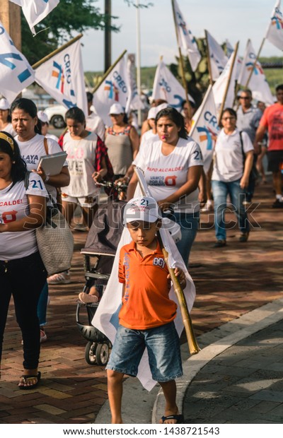 San Cristobal, Galapagos - March 2019: Local\
election rally with crowd of ecuadorian supporters. Men, Women,\
children in white marching in procession for political\
demonstration. Local police,\
flags.