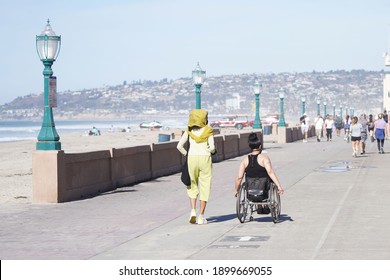 San Diego, CA USA - Jan 8 2021: Woman With Headscarf And Woman In Wheelchair Walk On The Boardwalk In Mission Beach On A Sunny Afternoon                               