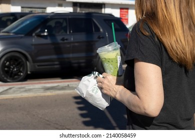 San Diego, CA, USA - Mar 24, 2022: A woman holds a cup of Starbucks iced coffee and a takeout bag in her hand on the streets in San Diego, California.