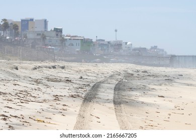 San Diego, CA, USA - May 14, 2022: Tire tracks on the sand beach at the Border Field State Park in San Diego, California, with the border fence between the U.S. and Mexico in the blurry background.