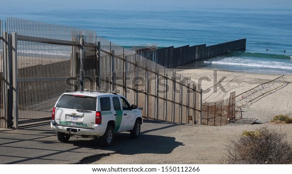 San Diego, CA / USA - November 3, 2019: A Border Patrol\
car drives along the tall fence at the US- Mexican border in San\
Diego\'s Border Field State Park.                             \
