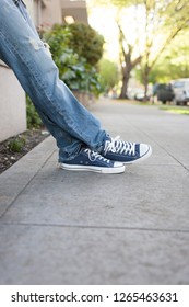 San Francisco, CA - July 23, 2012: Young Man Wearing Blue Jeans And Blue Converse Shoes Standing On The Sidewalk, Leaning On The Fence. 