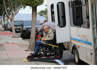 San Francisco, California, USA - December 24, 2015: Old man in a wheelchair is assisted to get off a van using a lift.