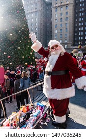 San Francisco, California/USA-12/8/2018: Santa Con At Union Square Park, Santa Claus Standing, Posing And Looking  Cheerful In Front Of Toys For Toys For Tots Drive Near The Crowds And Christmas Tree