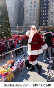 San Francisco, California/USA-12/8/2018: Santa Con At Union Square Park, Santa Claus Standing, Posing And Looking  Cheerful In Front Of Toys For Toys For Tots Drive Near The Crowds And Christmas Tree