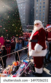 San Francisco, California/USA-12/8/2018: Santa Con At Union Square Park, Santa Claus Standing, Posing And Looking  Cheerful In Front Of Toys For Toys For Tots Drive Near The Crowds And Christmas Tree