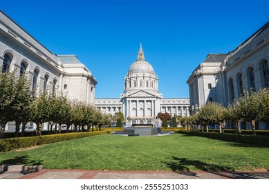 San Francisco City Hall stands with its grand Beaux Arts architecture and tall dome. A well maintained lawn and rows of trees enhance the civic center. - Powered by Shutterstock