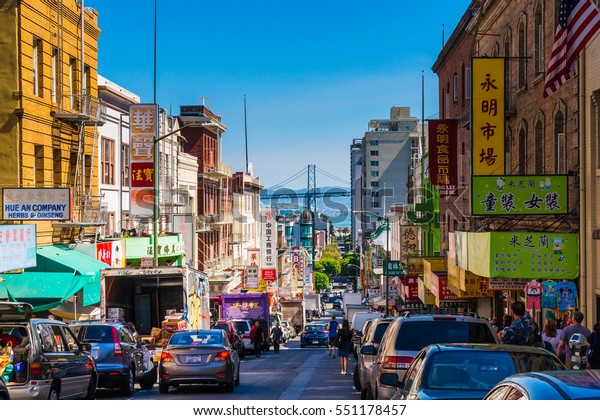 San Francisco -\
September 20, 2015: Downtown city life in a busy street of\
Chinatown San Francisco. View with many people, shops and cars -\
lookout to the Oakland Bay\
Bridge.
