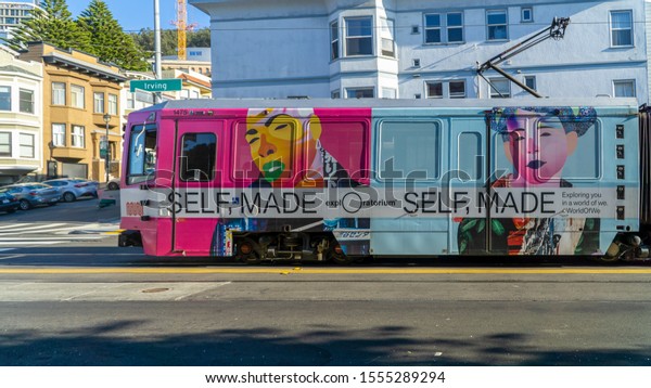 San Francisco,\
USA - August 2019: MUNI tramway with colorful exploratorium ads\
passing by irwing street