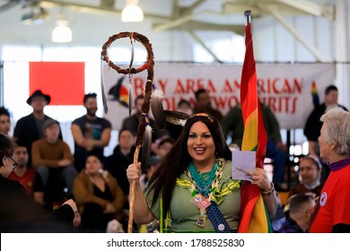 San Francisco, USA - February 08 2020: Native American Indian two spirit person holds a traditional Grand Entry eagle staff and rainbow flag at powwow