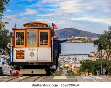 San Francisco, USA - January 21, 2020: Tourists riding the iconic cable car at the top of Hyde Street, with the famous Alcatraz Island in background