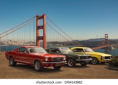 San Francisco. Year 2018: Front View Of Three Muscle Cars. Two Ford Mustang And One Chevrolet Camaro. Golden Gate Bridge In Background.