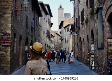 San Gimignano, Italy - October 17, 2019: Woman Wearing Fedora Walking Down Crowded Street In Ancient Medieval Town