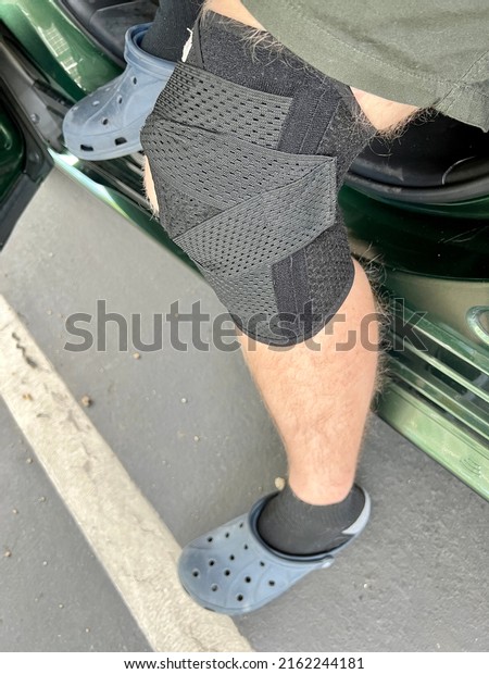 San Jose, CA - May 19,\
2022: Man wearing black knee brace while sitting sideways in the\
car, closeup. 