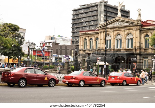 San Jose, Costa Rica - August 18, 2015: Classic red\
taxi cars are parked in front of the National Theater of Costa\
Rica, the main tourists attraction of the capital, on August 18,\
2015 in San Jose