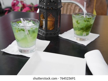 San Juan, Puerto Rico - Two Alcoholic Beverages Are Sitting On A Table Next To A Lantern And A Square Plate. The Beverages Are Set On Cocktail Napkins.