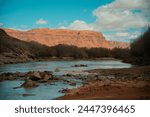 San Juan River flowing near Bluff Utah, desert wash pushing boulders into the river with large fluffy clouds blanketing the sky