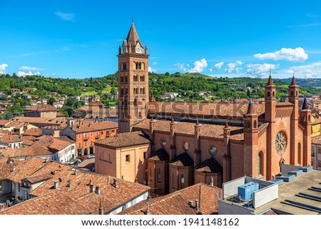San Lorenzo Cathedral (aka Duomo) among old houses with red roofs in Old Town as green hills on background in Alba, Piedmont, Northern Italy.