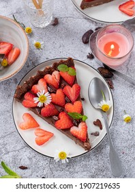 San Valentine Chocolate Raw Tart with strawberries and camomile flowers, served in white desserts plates over grey surface.