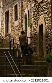 SAN VICENTE DE LA BARQUERA, SPAIN, JULY, 13, 2022: Man On A Bicycle Climbing Stairs In A Rural Town Of Cobblestone Streets. Concept Of Transport, Bike Lane, Infrastructure