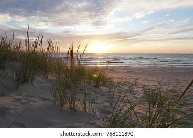 Sand with beach grass in foreground, clouds and sun with blue sky, lake in background