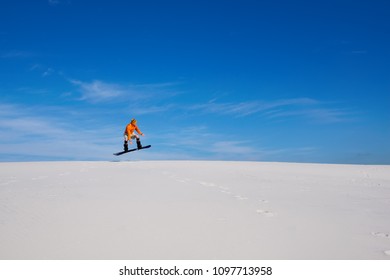 Sand boarding in desert at sunny day. Man is flying on a snowboard over sand dunes against of blue sky. Wide angle, side view. - Shutterstock ID 1097713958