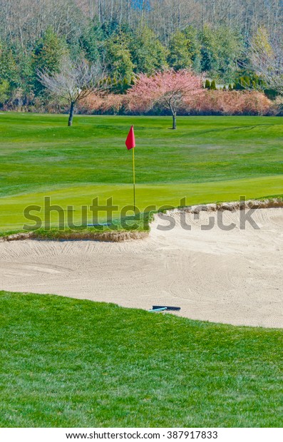 Sand bunker and the red flag at the beautiful\
golf course.