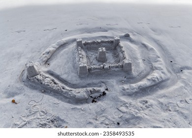 Sand Castle With Outer Ring Eroded By Water On Beach With Footprints