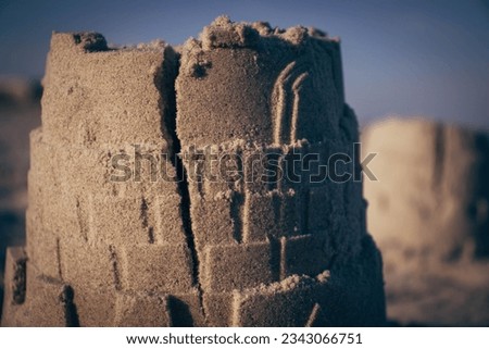 A sand castle tower with a big crack running down it on a beach