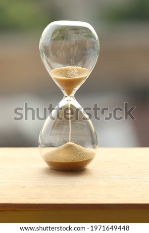 Sand clock measuring time with orange sky in evening time over city blurred background, yellow sand falling down in hourglass old classic timer.