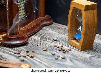 Sand Clock And Scattered Grains Of Roasted Coffee On A Vintage Rough Wooden Background. Sandglass, Hourglass Or Egg Timer On Wooden. Antique Style Wooden Background.