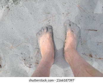 Sand Covered Toes And Feet In The Sand At A Beach. The Man's Feet Are Sitting At The Bottom Of A Whole In The Sand.