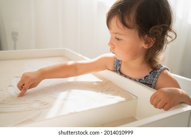 Sand drawing table for children. A little girl draws with her finger on a light sand table. Creative development in young children. - Powered by Shutterstock