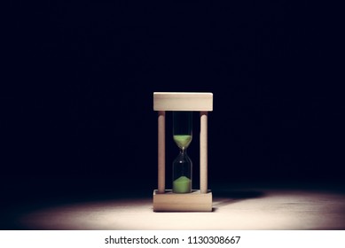 sand glass on wood floor ,  dark background lighted with snoot