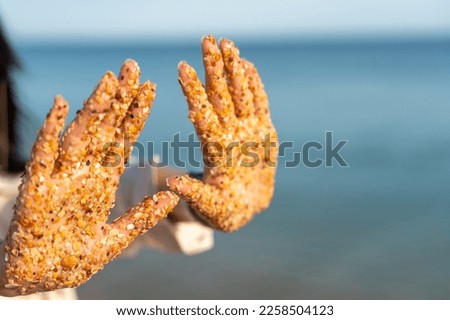 Sand hand sea. Small pieces of shells sand stuck to the palms of a woman against the backdrop of the sea and blue sky.