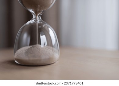 Sand passes through the bulbs of an hourglass, measuring the passage time in a countdown to the deadline, on a dark background with copy space.